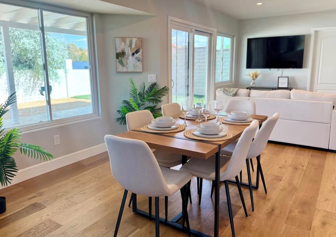 A dining area with a wooden table set for four, surrounded by white chairs.