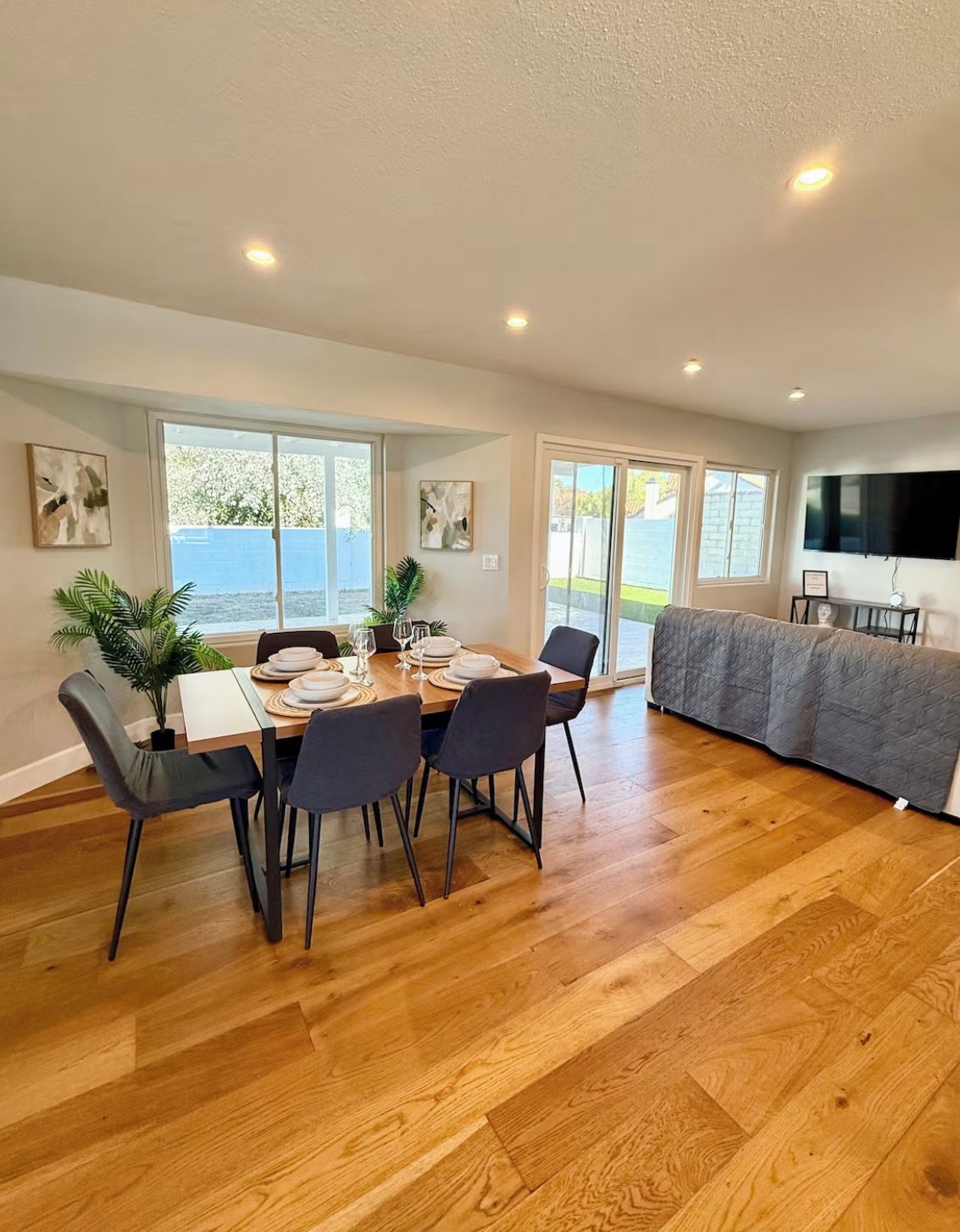 A dining area with a table set for four, a sofa, and a TV mounted on the wall.