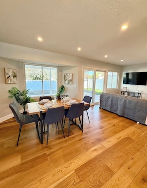 A dining area with a table set for four, a sofa, and a TV mounted on the wall.