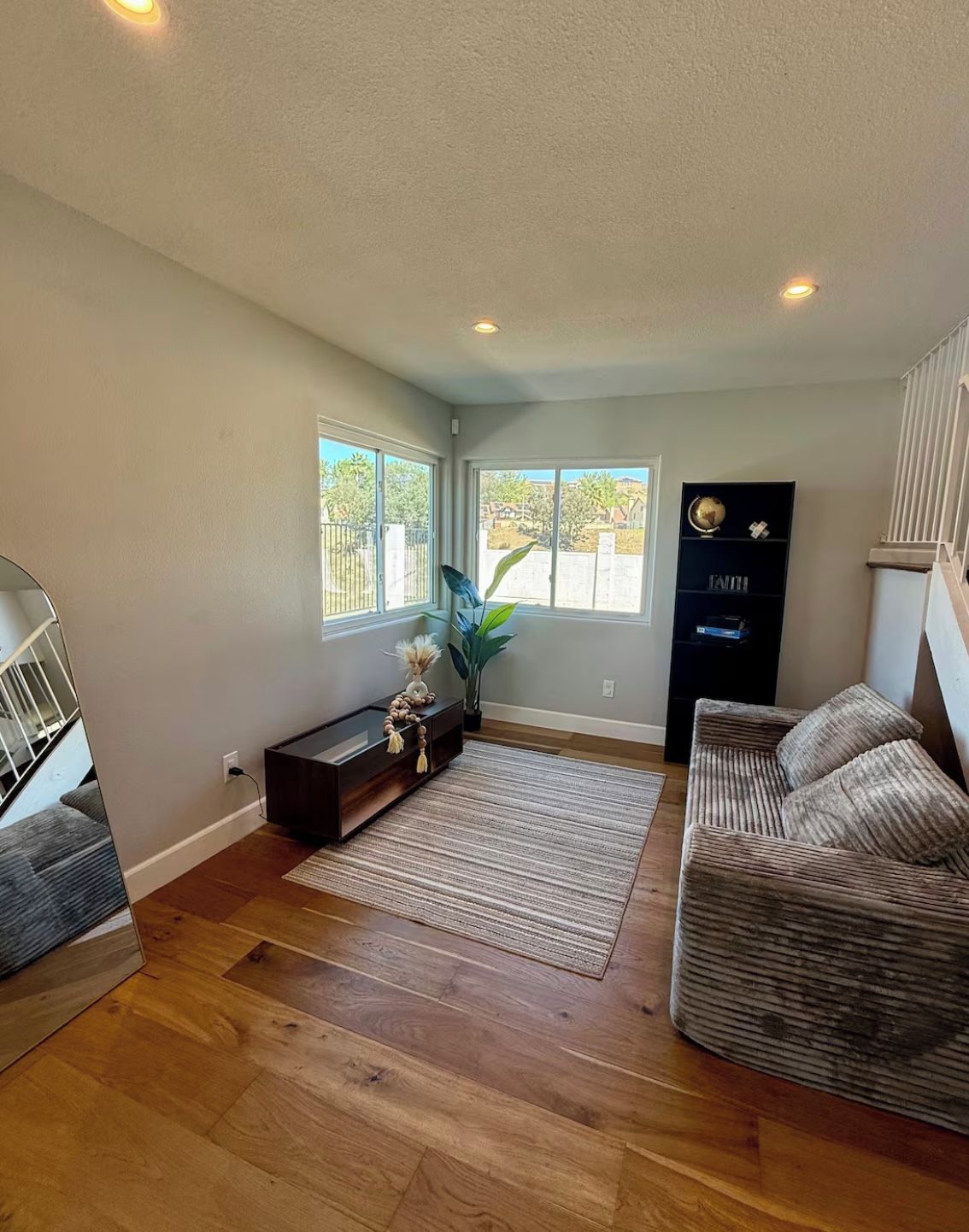 A spacious living room with hardwood flooring, a sofa, a coffee table, and a bookshelf.