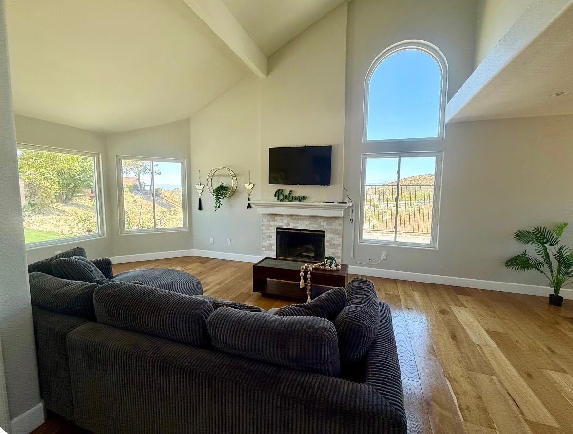 A spacious living room with a fireplace, large windows, and a television.