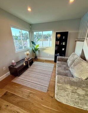 A living room with a sofa, a coffee table, a bookshelf, and a large window. - Luxury Scenic Retreat, Spacious Home, Elegant Comfort & Stunning Views (Santa Clarita)