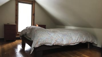 Une chambre à coucher avec un lit, une commode en bois et une fenêtre laissant entrer la lumière naturelle.