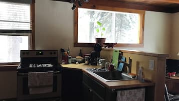 Une cuisine compacte dotée d’un four encastré, d’un évier et d’une fenêtre donnant sur les arbres.