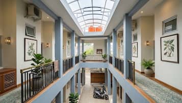 A multi-level atrium with a glass ceiling, potted plants, and a scooter parked in the center.