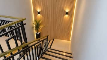 Una escalera con piso a rayas blancas y negras, una planta en maceta y lámparas fijadas a la pared.