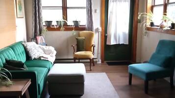 A living room with a green sofa, a yellow armchair, a blue armchair, a ceiling fan, and a door with a curtain.
