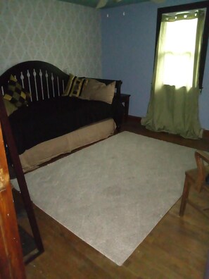 Een kamer met een bed, een raam met gordijnen en een houten vloer.