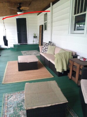 Een overdekt terras met een bank, kussens en een bijzettafeltje.