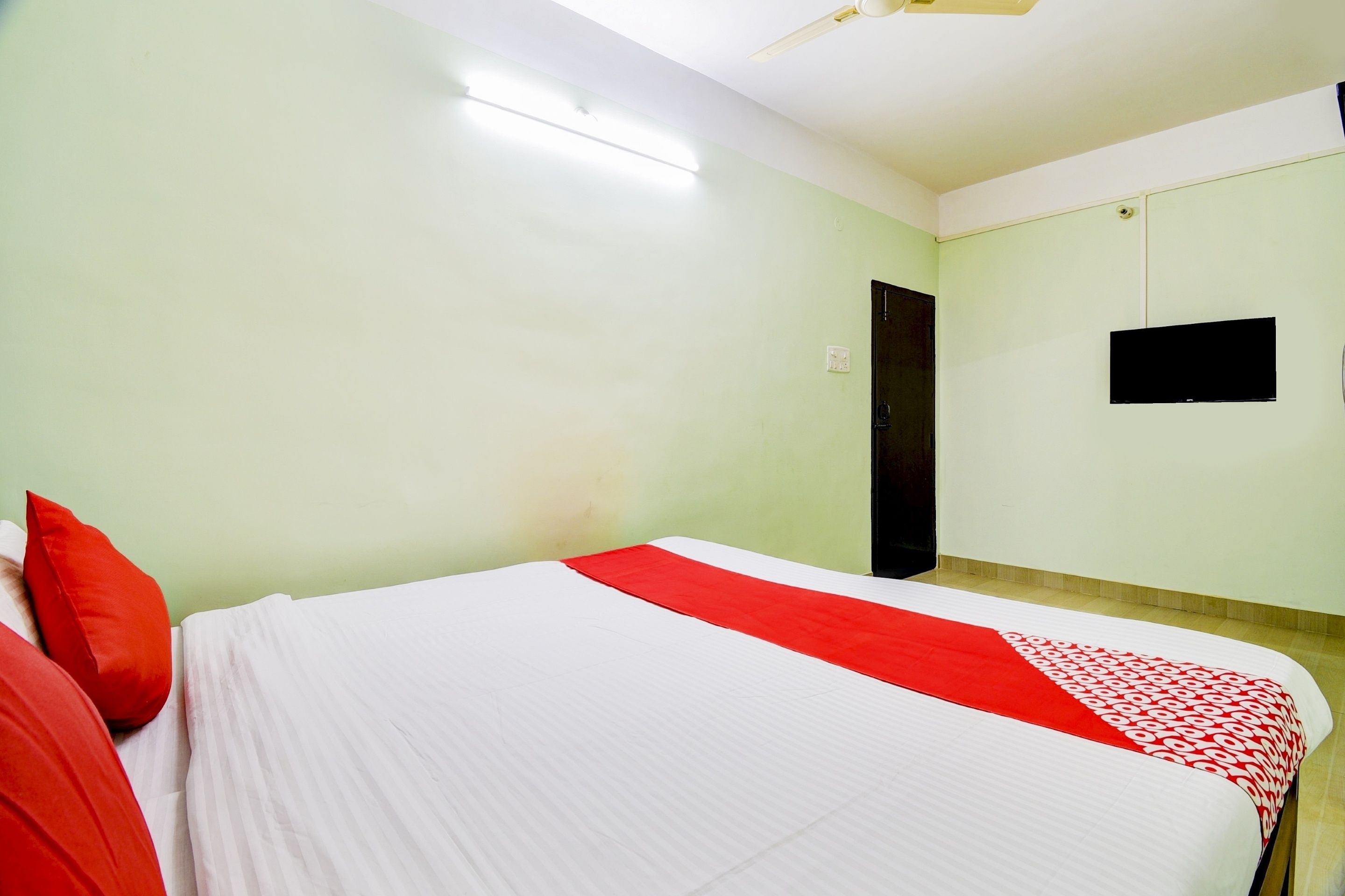 Una habitación con una cama, una puerta, un televisor montado en la pared y un ventilador de techo.