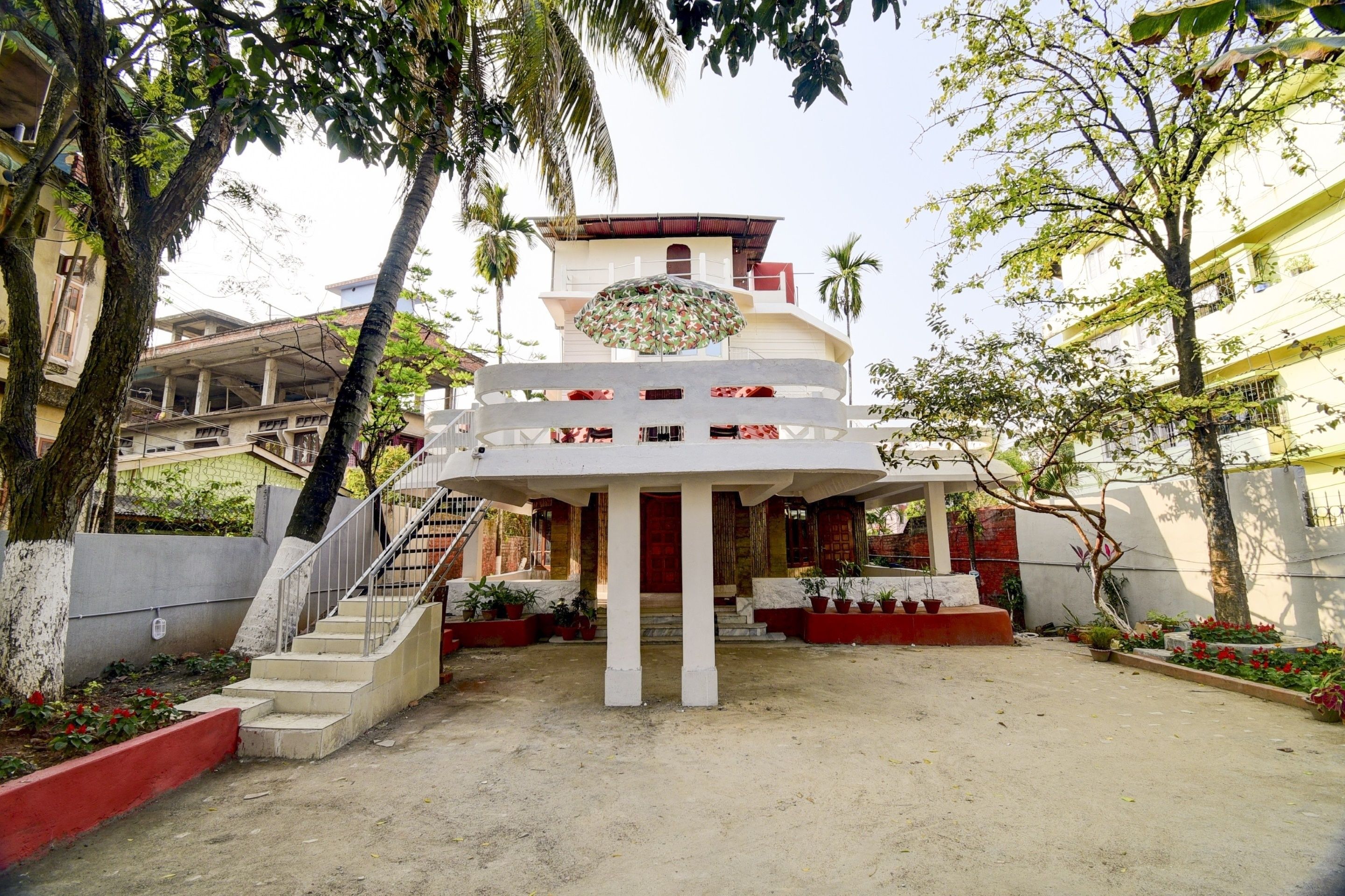 Um edifício com vários níveis e uma escadaria central, cercado por vegetação e outras construções.