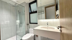 Ein modernes Badezimmer mit Duschkabine aus Glas, Toilette und Waschbecken mit Spiegel darüber.