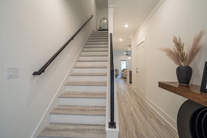 A staircase with a handrail leading to a landing, a wall-mounted light fixture, and a wooden floor.