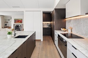 A modern kitchen with a marble countertop, wooden cabinets, and a built-in oven. - Premium Matakana Getaway Close to Matakana Village (Matakana)