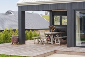 A covered outdoor patio with a wooden table and chairs, a grill, and potted plants. - Premium Matakana Getaway Close to Matakana Village (Matakana)