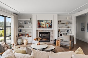 A modern living room with a fireplace, bookshelves, and a large window. - Premium Matakana Getaway Close to Matakana Village (Matakana)