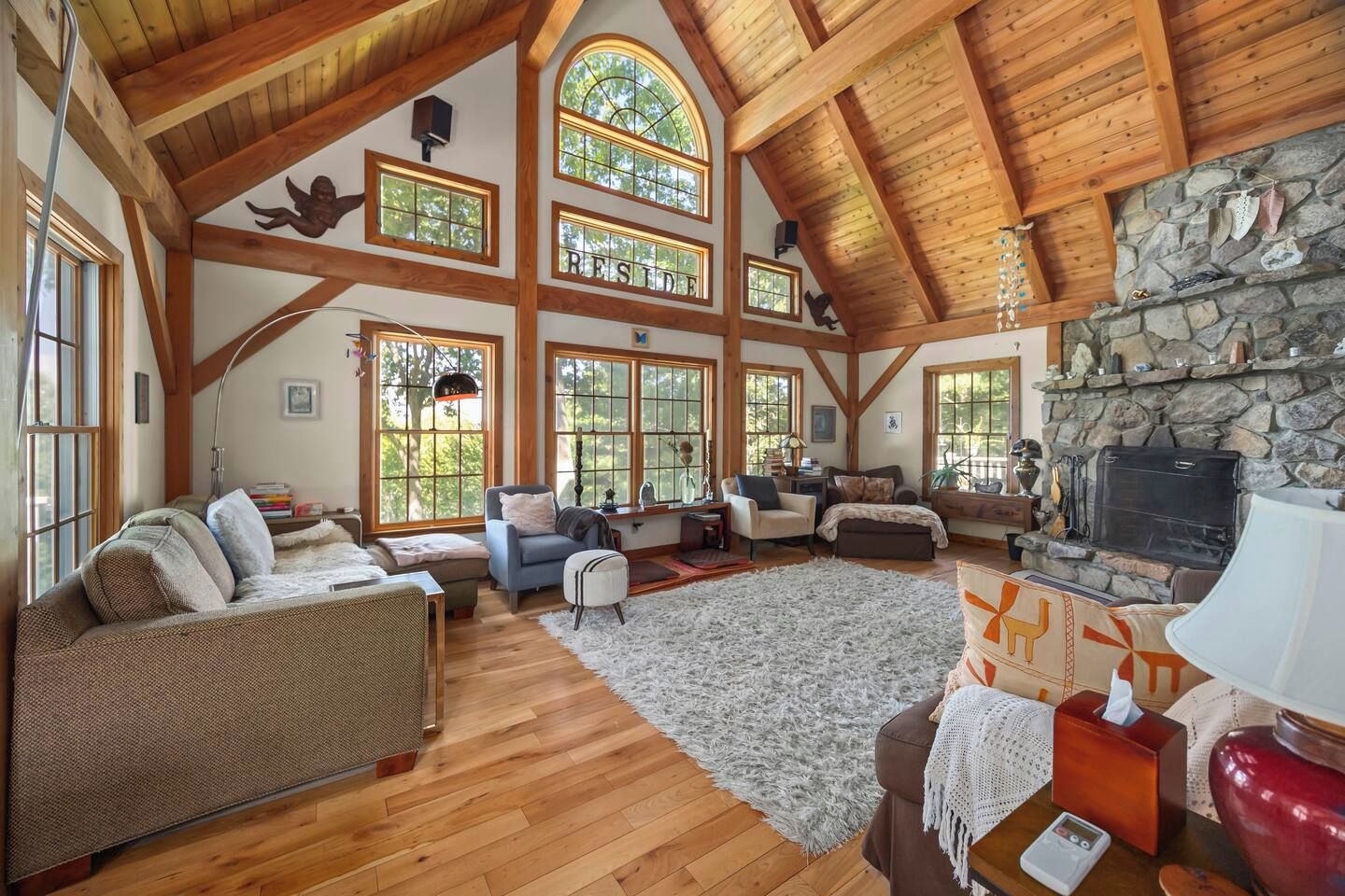 A spacious living room with wooden beams, large windows, a stone fireplace, and a cozy seating area.