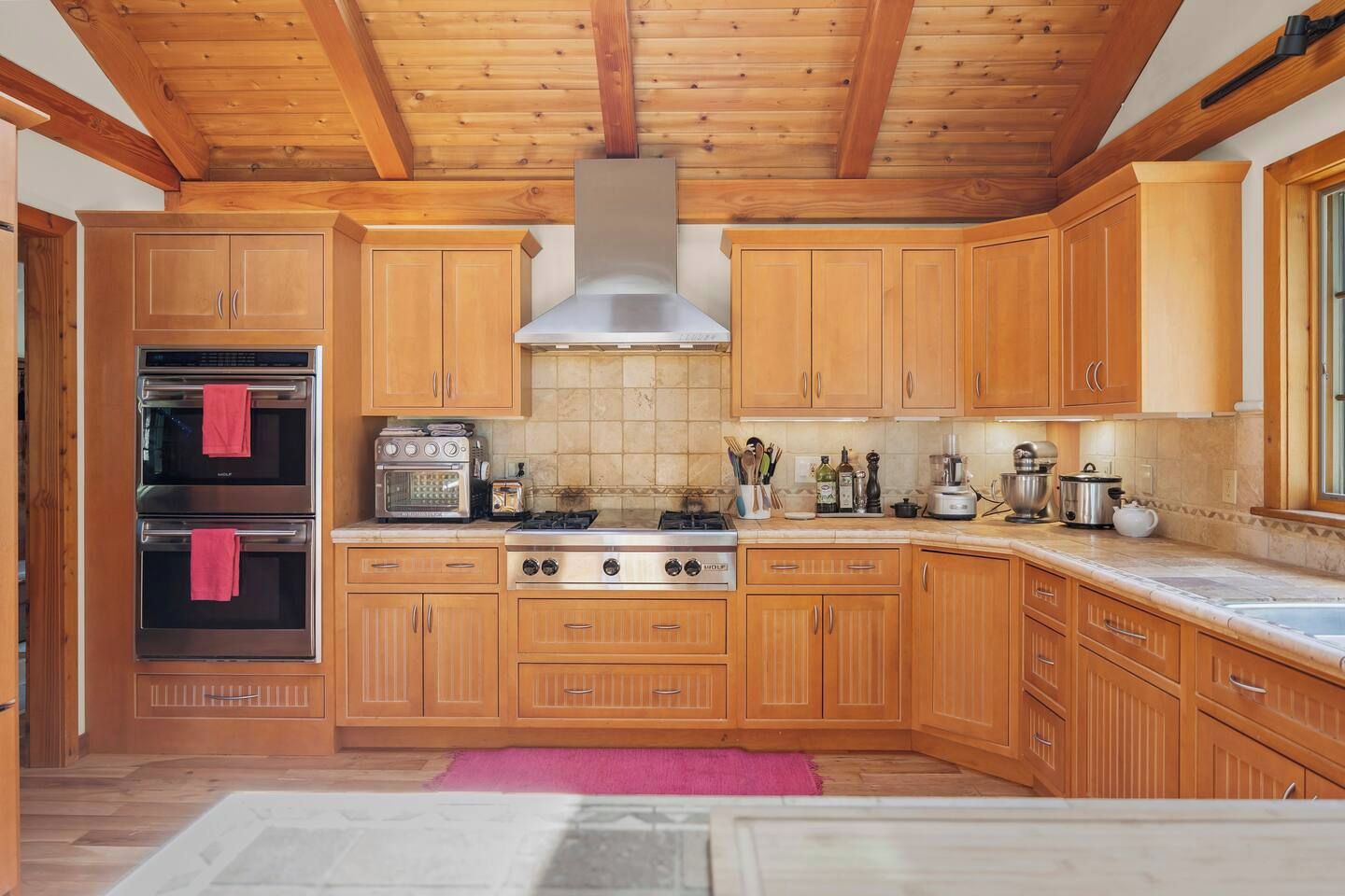Una cocina con gabinetes de madera, estufa a gas, horno y campana extractora.