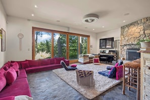 A modern living room with a red sectional sofa, a grey pouf, and a piano. - Lavish Sanctuary Main House-Hot Tub Copake Lake (Craryville)