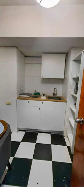 Eine kleine Küche mit schwarz-weiß kariertem Boden, einem Spülbecken und Schränken.