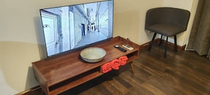 Ein Holz-TV-Schrank mit einer Schale und einer Fernbedienung, ein Sessel und ein Fernseher, der eine Straßenszene zeigt.