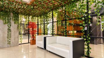 Un interior moderno con un sofá blanco, una planta en maceta roja y plantas trepadoras verdes.
