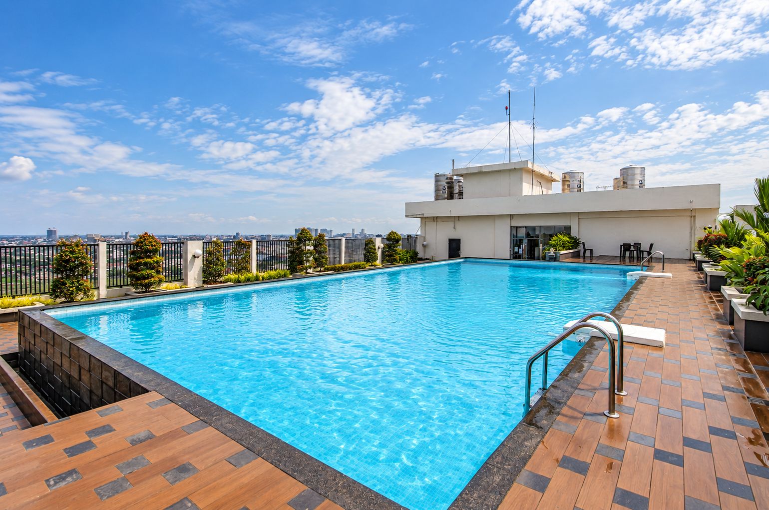 Una piscina en la azotea con vista al horizonte de la ciudad, rodeada por una cerca y plantas en macetas.