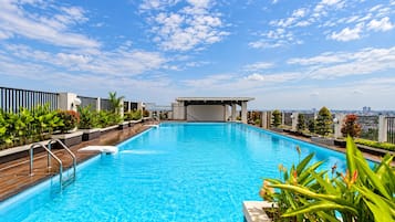 Una piscina en la azotea con vistas despejadas del horizonte urbano, rodeada de follaje y arquitectura moderna.