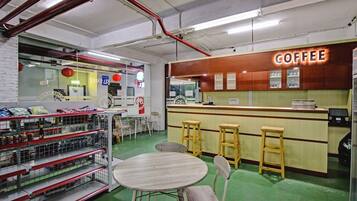 Interior de una cafetería con mostrador, taburetes y estantes llenos de productos.