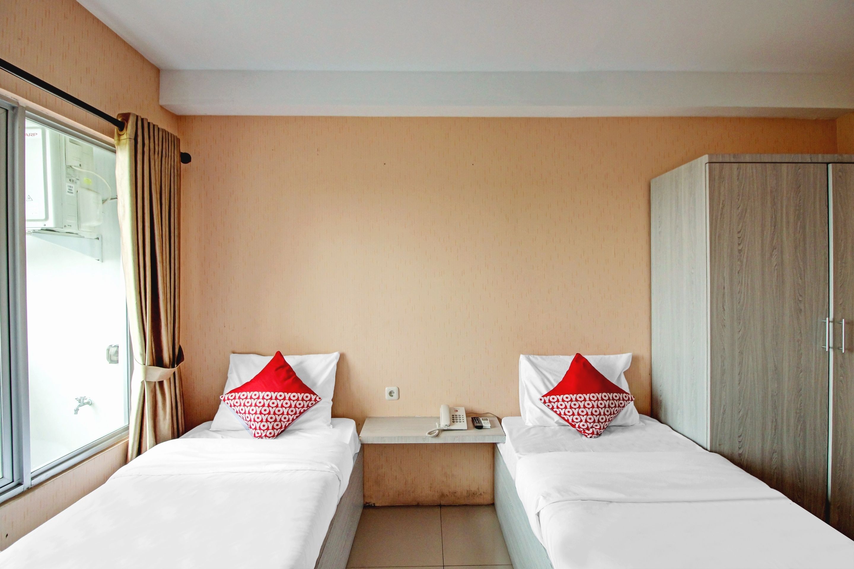 Habitación de hotel con dos camas individuales, un armario, una mesita de noche con teléfono y control remoto, y una ventana con cortinas.