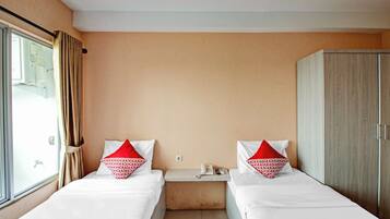 Habitación de hotel con dos camas individuales, un armario, una mesita de noche con teléfono y control remoto, y una ventana con cortinas.