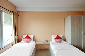 A hotel room with two single beds, a wardrobe, a bedside table with a phone and a remote control, and a window with curtains. - Collection O Dassa (Medan)