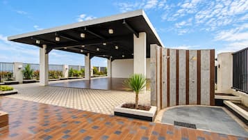 Un espacio al aire libre cubierto con piso de baldosas, una palmera y un edificio moderno con techo inclinado.