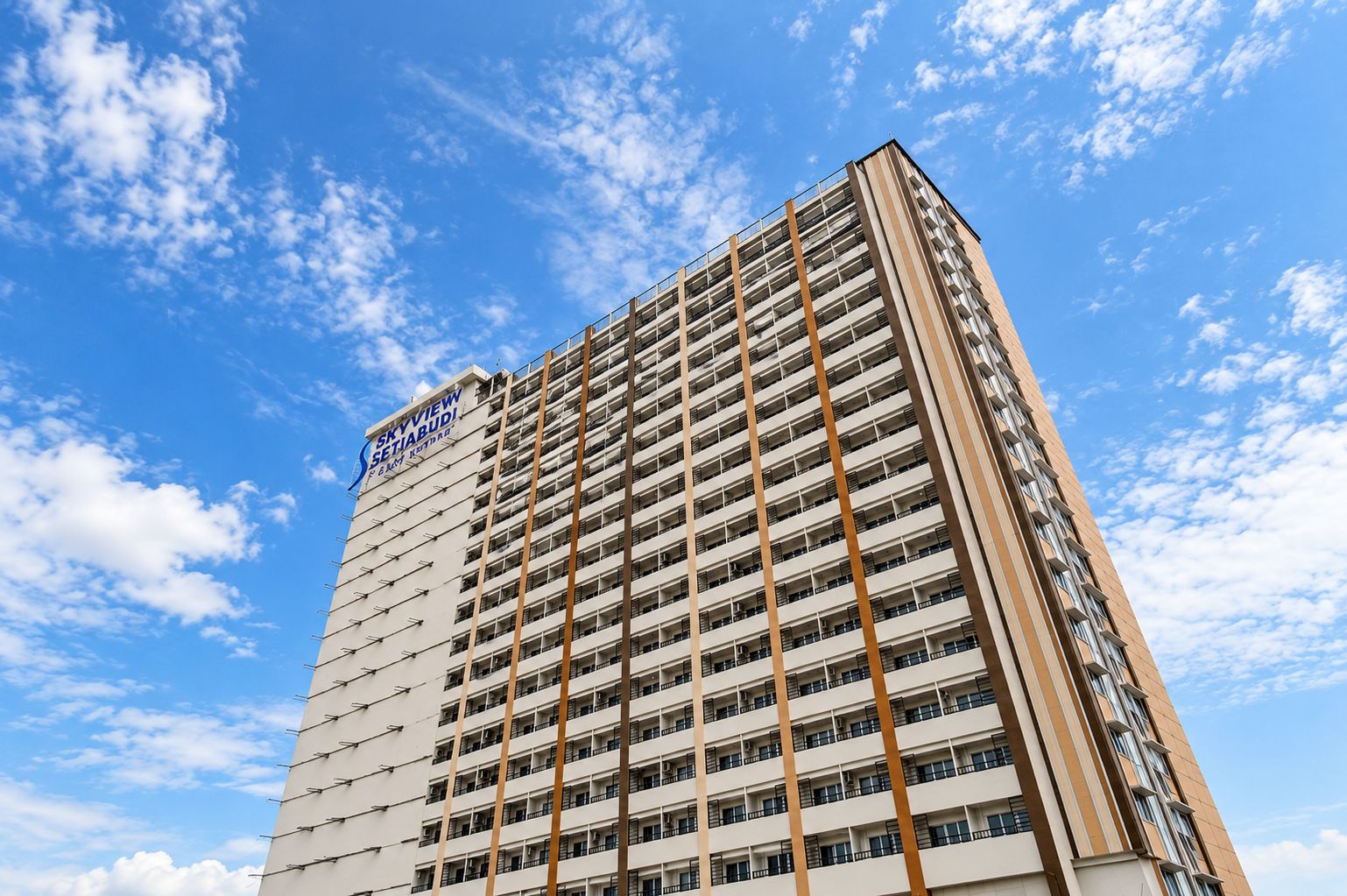 Un hotel de gran altura con varios pisos, un cartel llamativo en la parte superior y un cielo azul despejado con nubes al fondo.