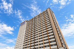 A high-rise hotel with multiple floors, a prominent sign at the top, and a clear blue sky with clouds in the background. - Collection O Dassa (Medan)