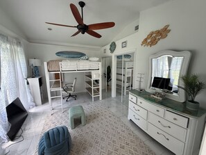 Een slaapkamer met een stapelbed, een bureau, een stoel, een dressoir, een spiegel en een plafondventilator.