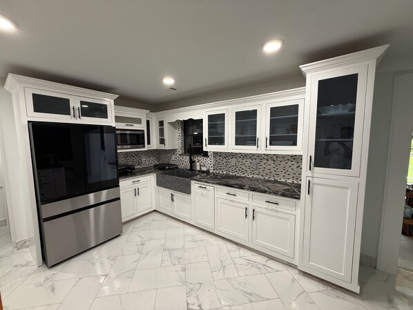 A modern kitchen with white cabinetry, a stainless steel refrigerator, and a granite countertop. - Spacious 1 acre property with a 6 bedrooms house in charming Brunswick with AC. (Brunswick)