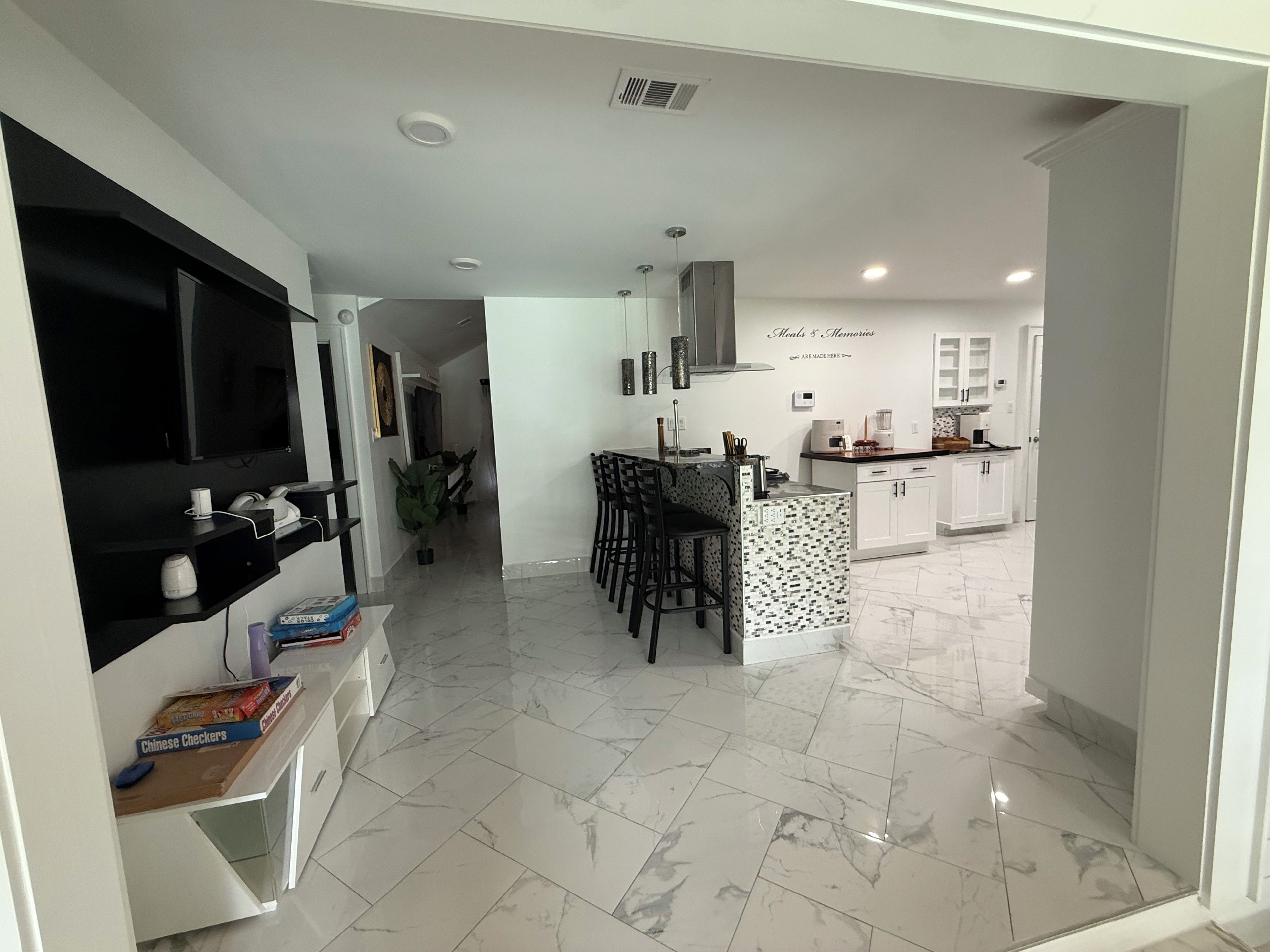 A modern kitchen with white cabinets, a dining area with bar stools, and a TV on a black stand.