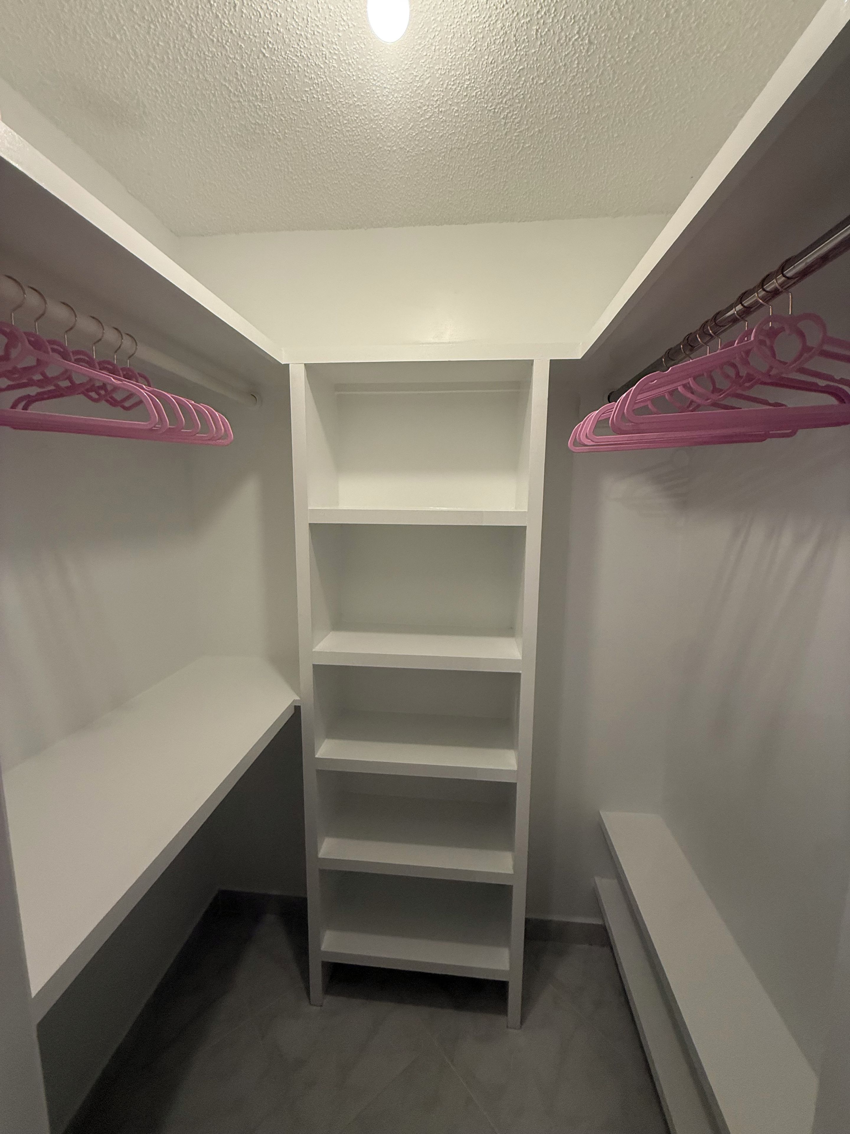 A walk-in closet with white shelving and pink hangers.