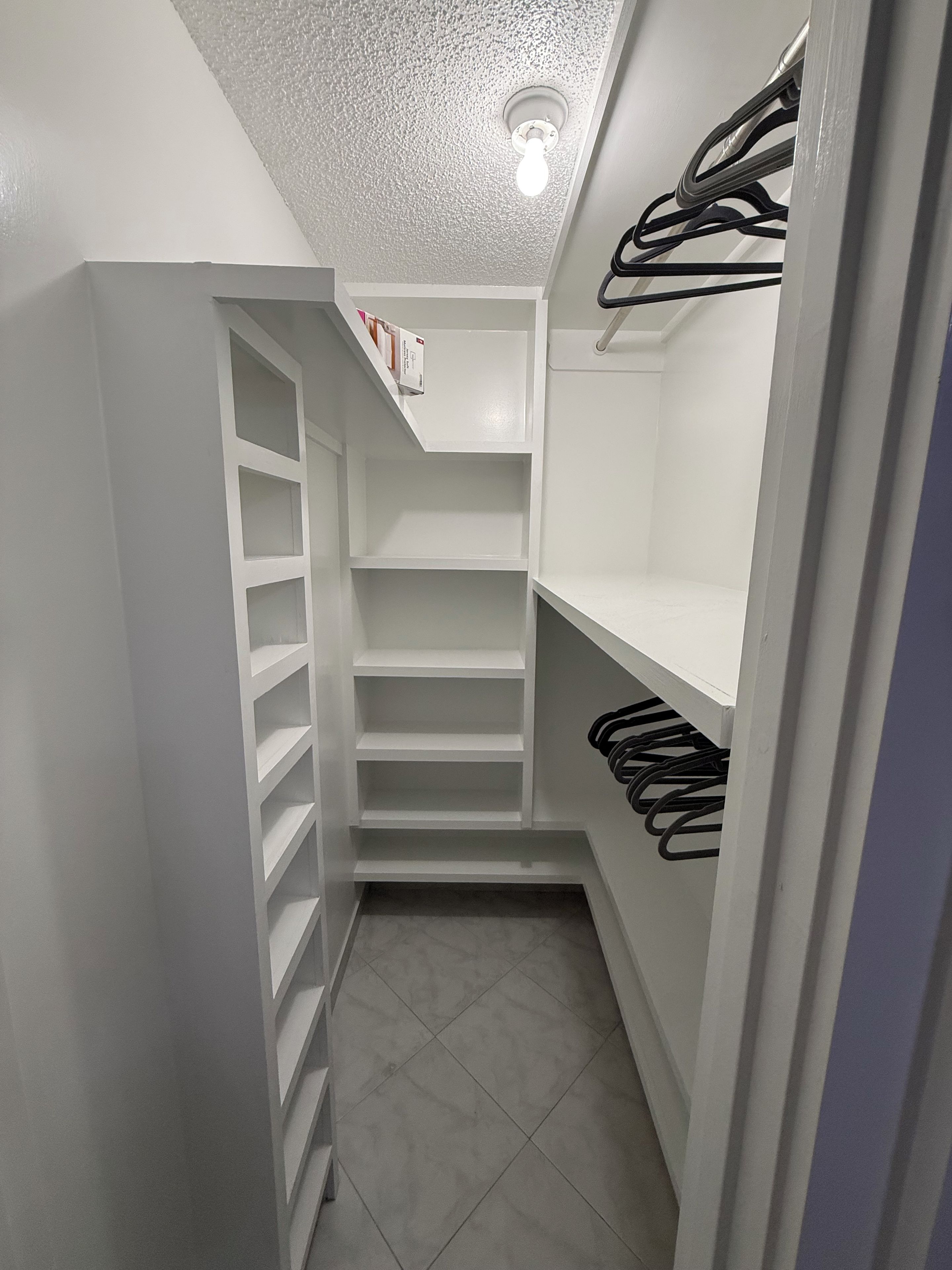 A narrow walk-in closet with white shelving and a hanging rod.