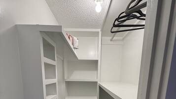 A narrow walk-in closet with white shelving and a hanging rod.
