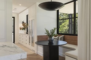 A modern interior with a marble countertop, a round black table, a sofa with cushions, and a large window with a view of trees. - The Pines Estate, Tallebudgera Valley (Tallebudgera Valley)