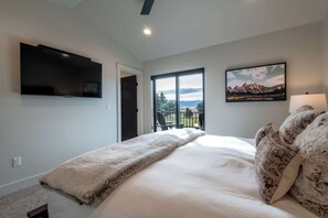 A bedroom with a bed, a TV mounted on the wall, a window with a view, and a painting. - Teton Homestead: Stone Peak Hideaway (Driggs)