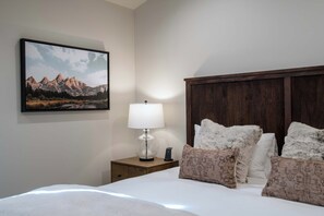 A hotel room with a bed, a nightstand, a lamp, and a framed picture on the wall. - Teton Homestead: Stone Peak Hideaway (Driggs)