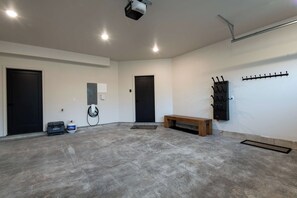 Una habitación amplia con suelo de hormigón, dos puertas negras, una banca, un calentador fijado a la pared y un proyector montado en el techo.