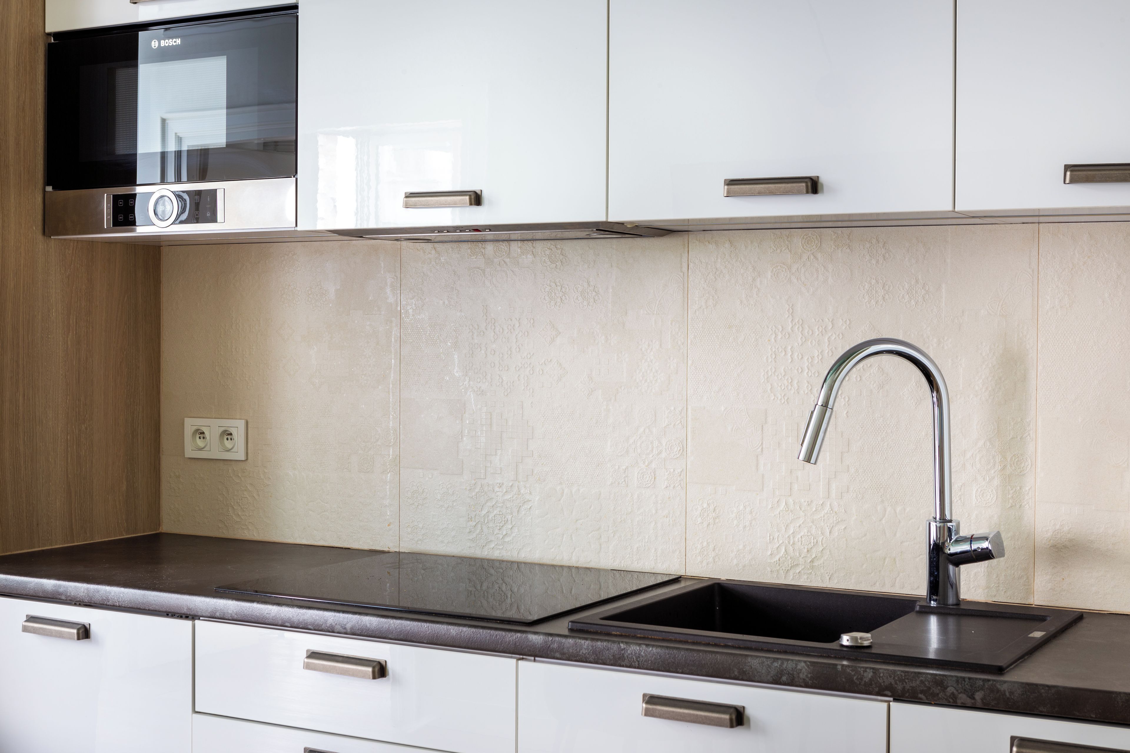 Cucina con lavello in acciaio inossidabile, un microonde Bosch e mobili bianchi.