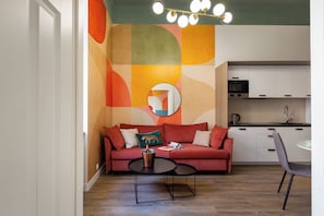 Una sala de estar moderna con un sofá rojo, una mesa de centro y una cocina con armarios blancos y un horno Bosch.