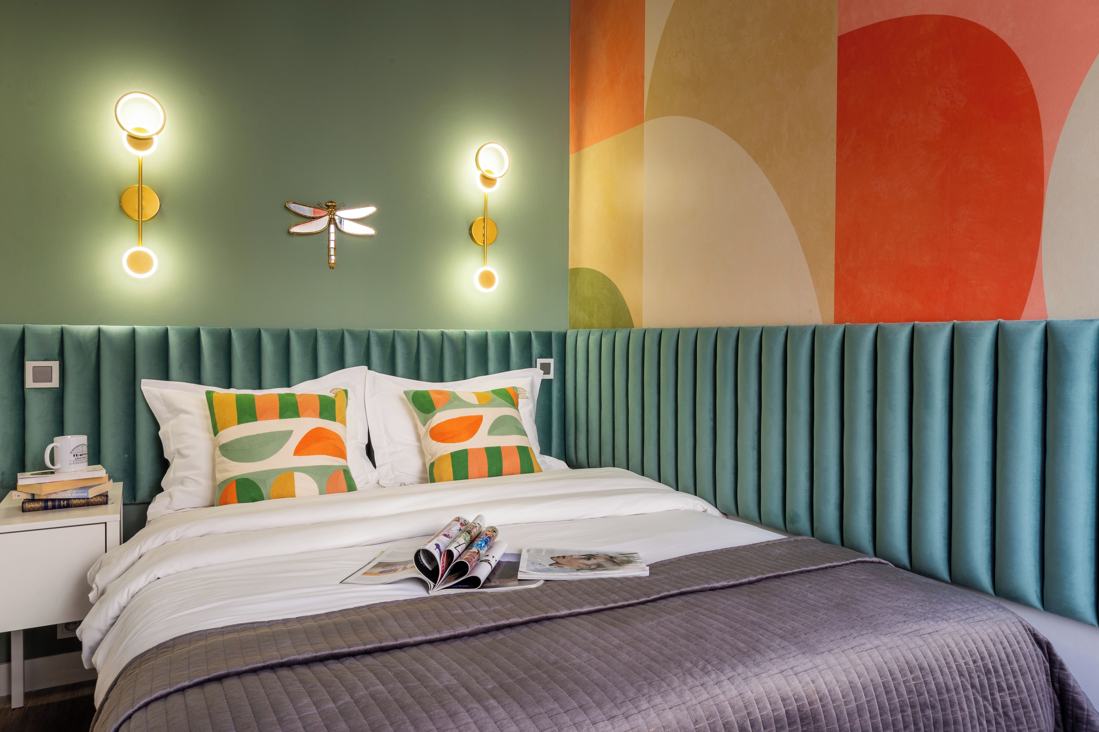 A modern bedroom with a teal upholstered headboard, a bed with white bedding, and a colorful abstract wall art piece.