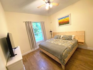 A bedroom with a wooden bed, a ceiling fan, a window with curtains, and a painting on the wall. - Winter Garden Butterfly Retreat - Trailside (Winter Garden)