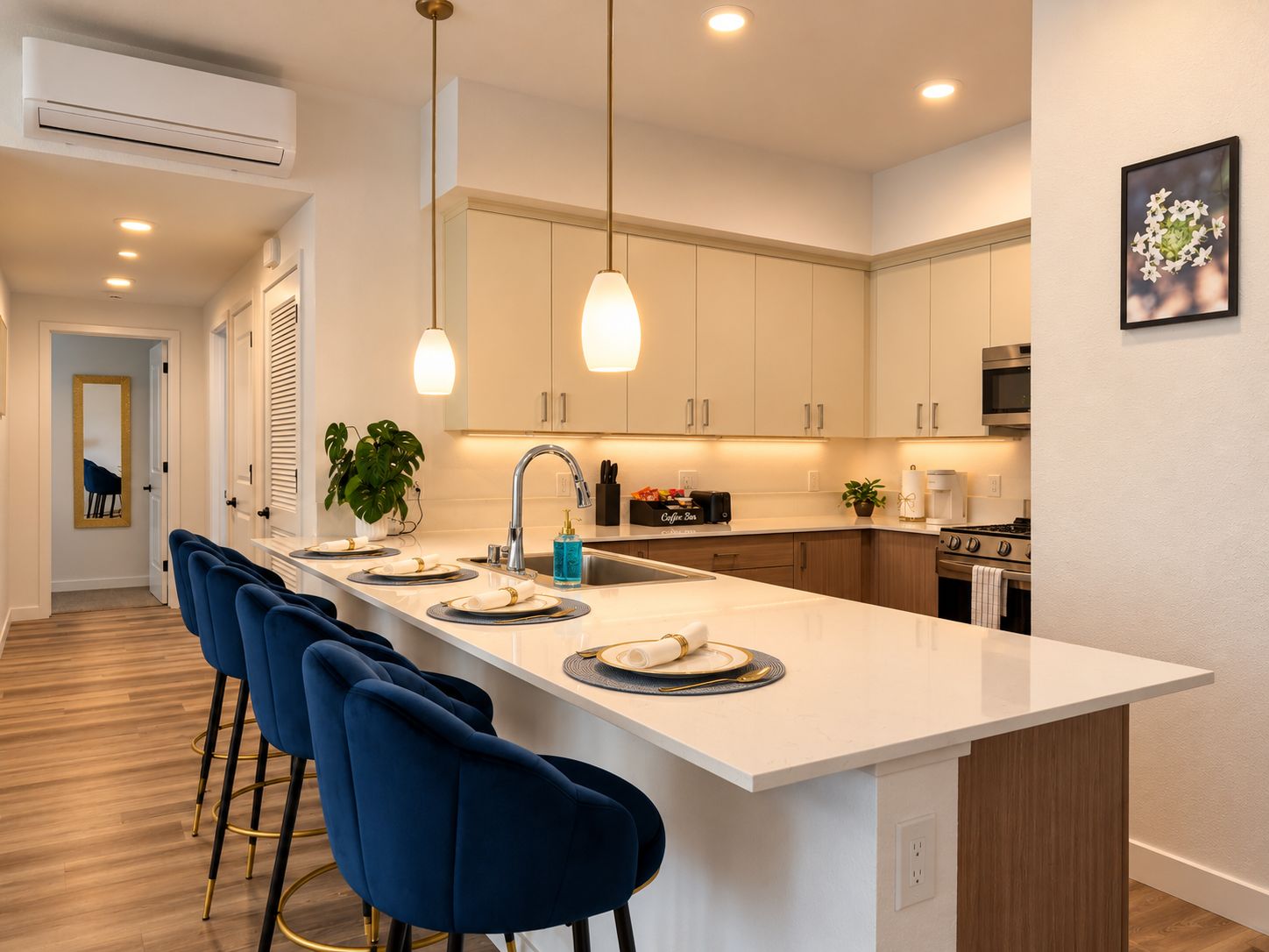 A modern kitchen with a central island, bar stools, pendant lighting, and a microwave.
